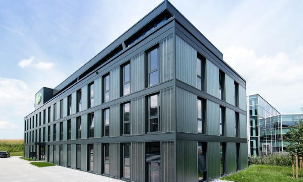 Moderne Bürogebäude mit Glasfassade und klaren Linien, umgeben von Bäumen und einem Gehweg