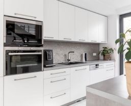 Helle, moderne Küche mit weißen Schränken und einem großen Fenster, das den Raum erhellt