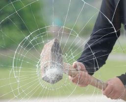 Ein Mann hält einen Hammer und zerbricht ein Glasfenster